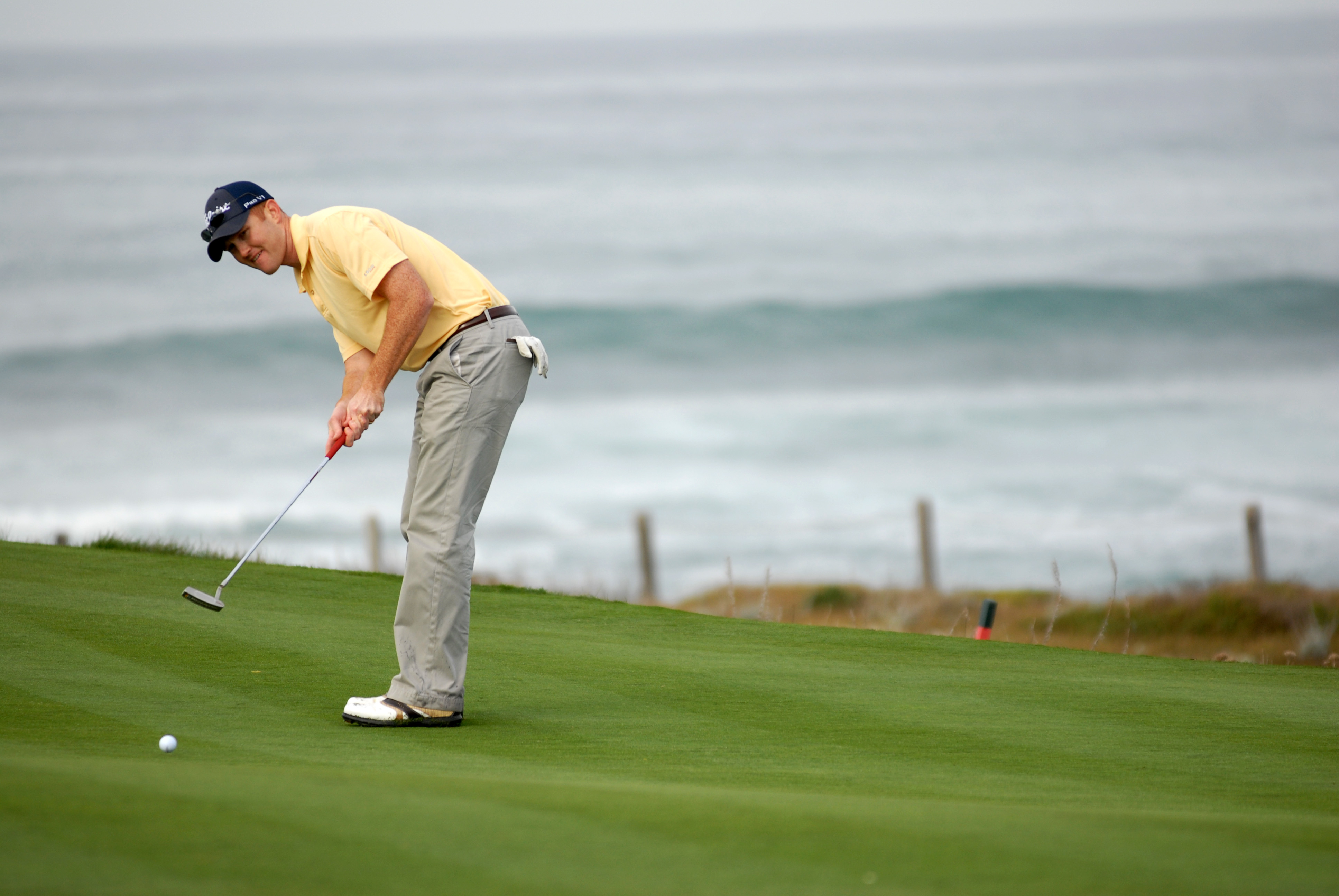 Golfer making putt by ocean on California course